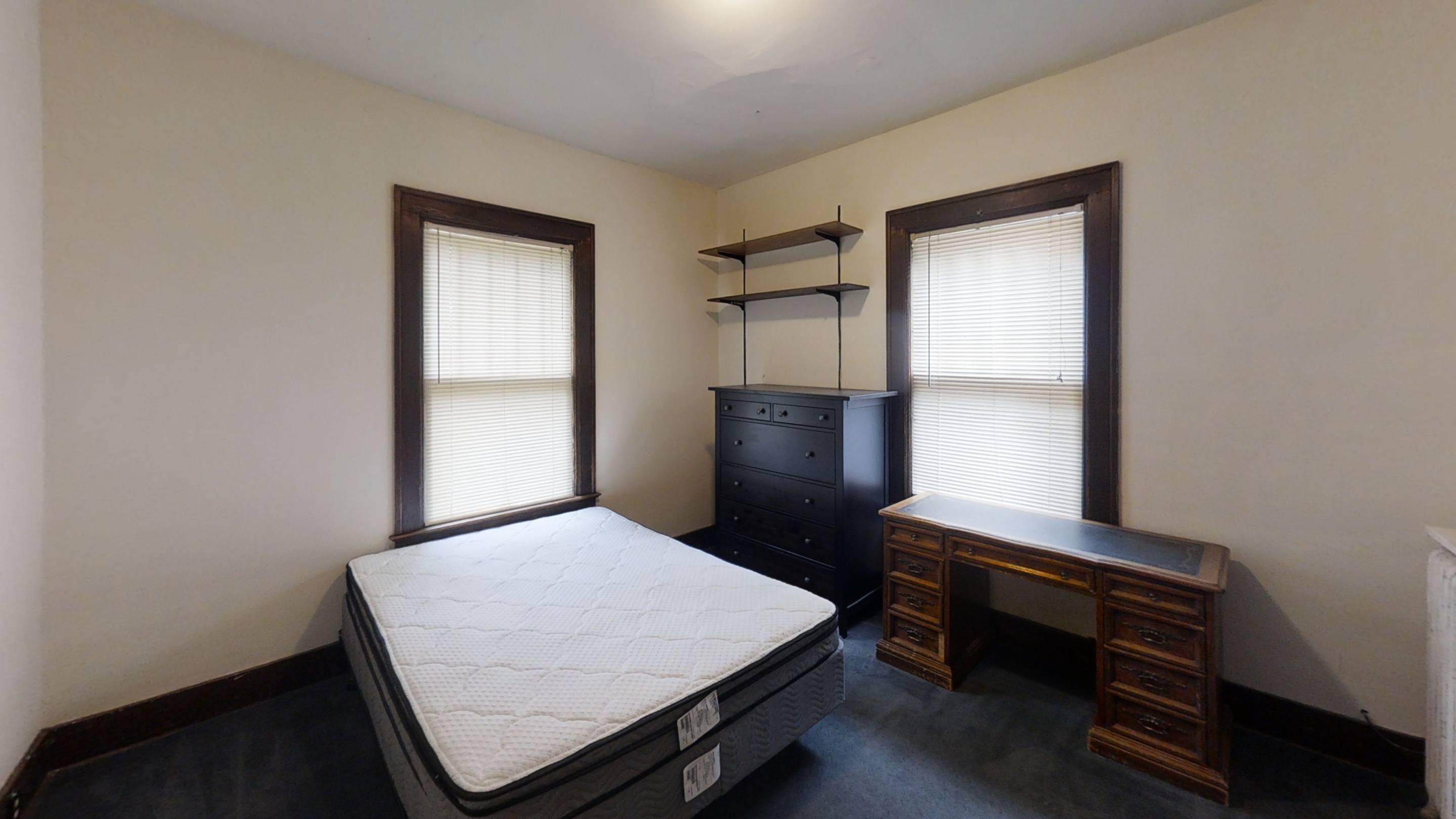 A bedroom with a bed, desk, and shelves.